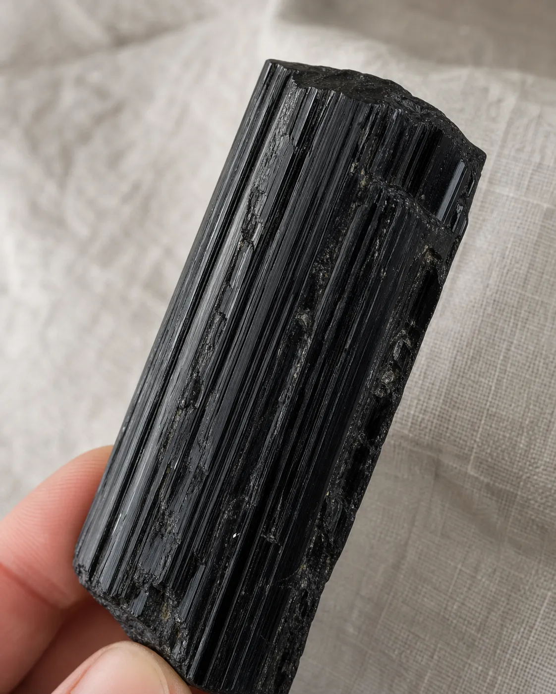 Raw black tourmaline specimen showing coherent habit, lengthwise structure, dark color, and readable surface detail