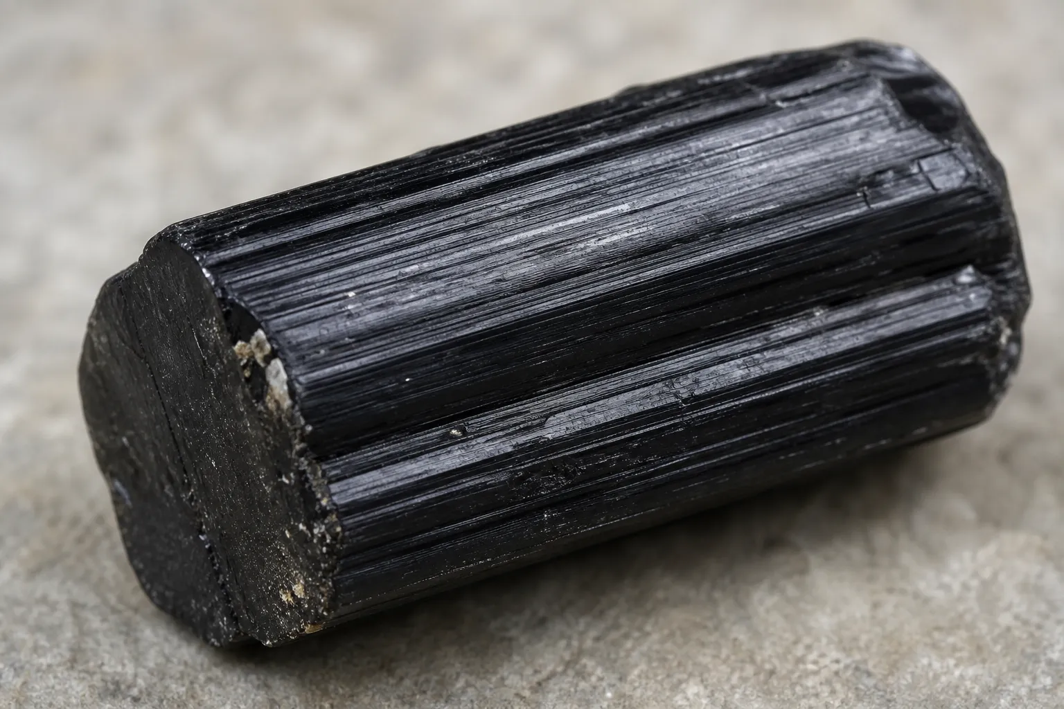 Raw black tourmaline crystal with lengthwise surface grooves along its prismatic body