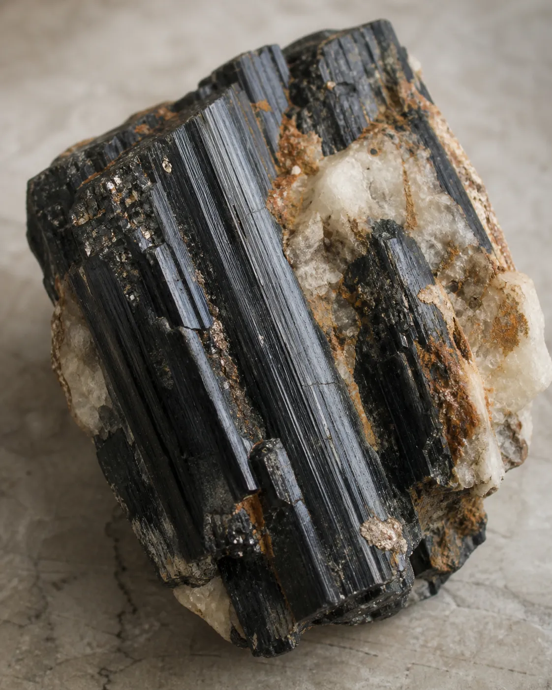 Raw black tourmaline with striations, broken faces, pale matrix, rusty coating, and small bright specks that cannot be identified by sight alone