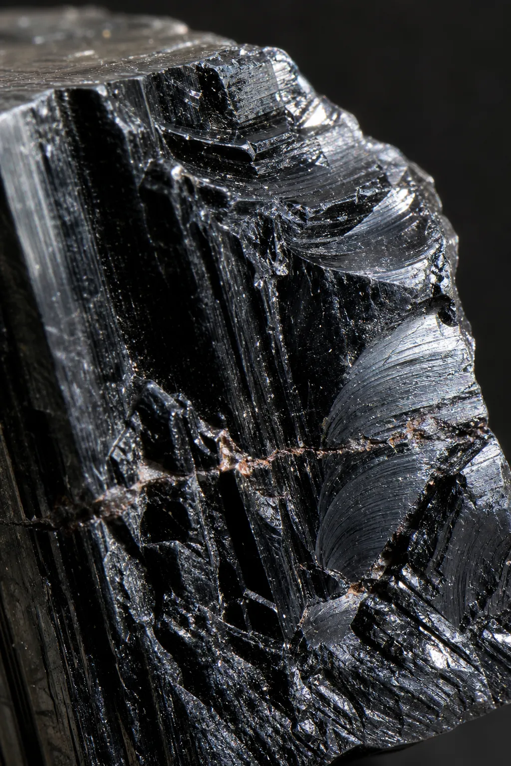 Close view of black tourmaline fracture surfaces with irregular areas and possible curved arcs