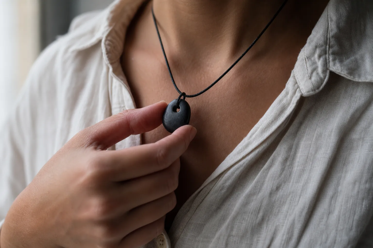 A hand lightly touching a matte stone necklace as a small cue for texture, weight, breath, posture, and transitions