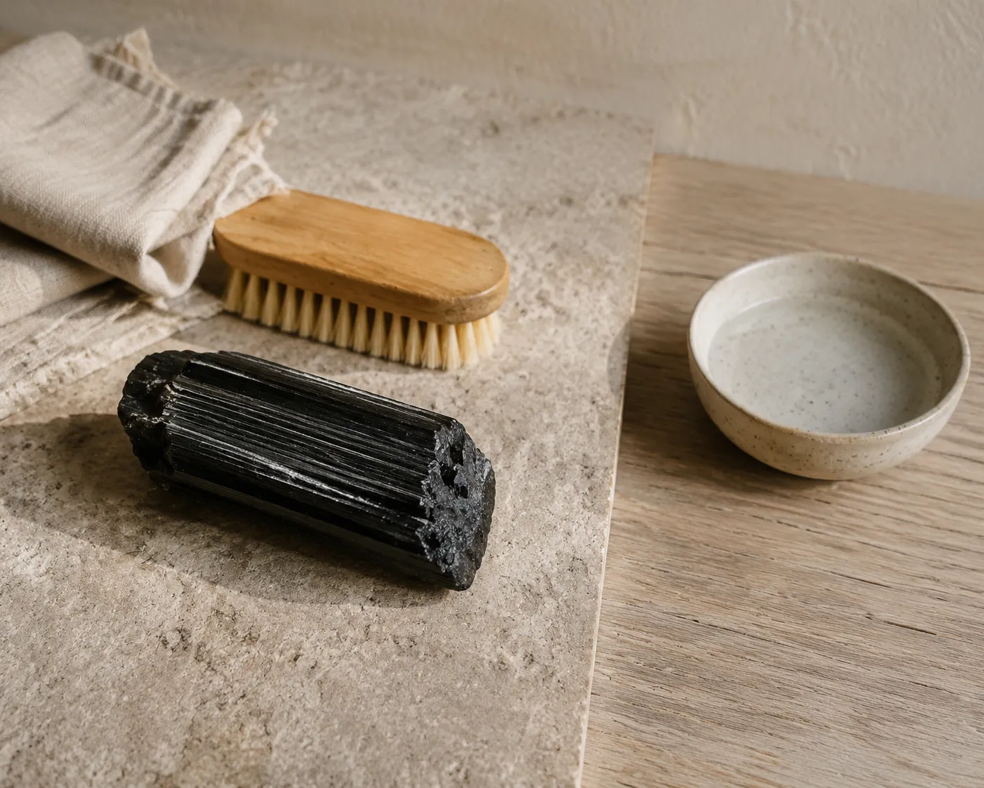 Raw black tourmaline on a dry care surface beside a soft brush and a small water dish