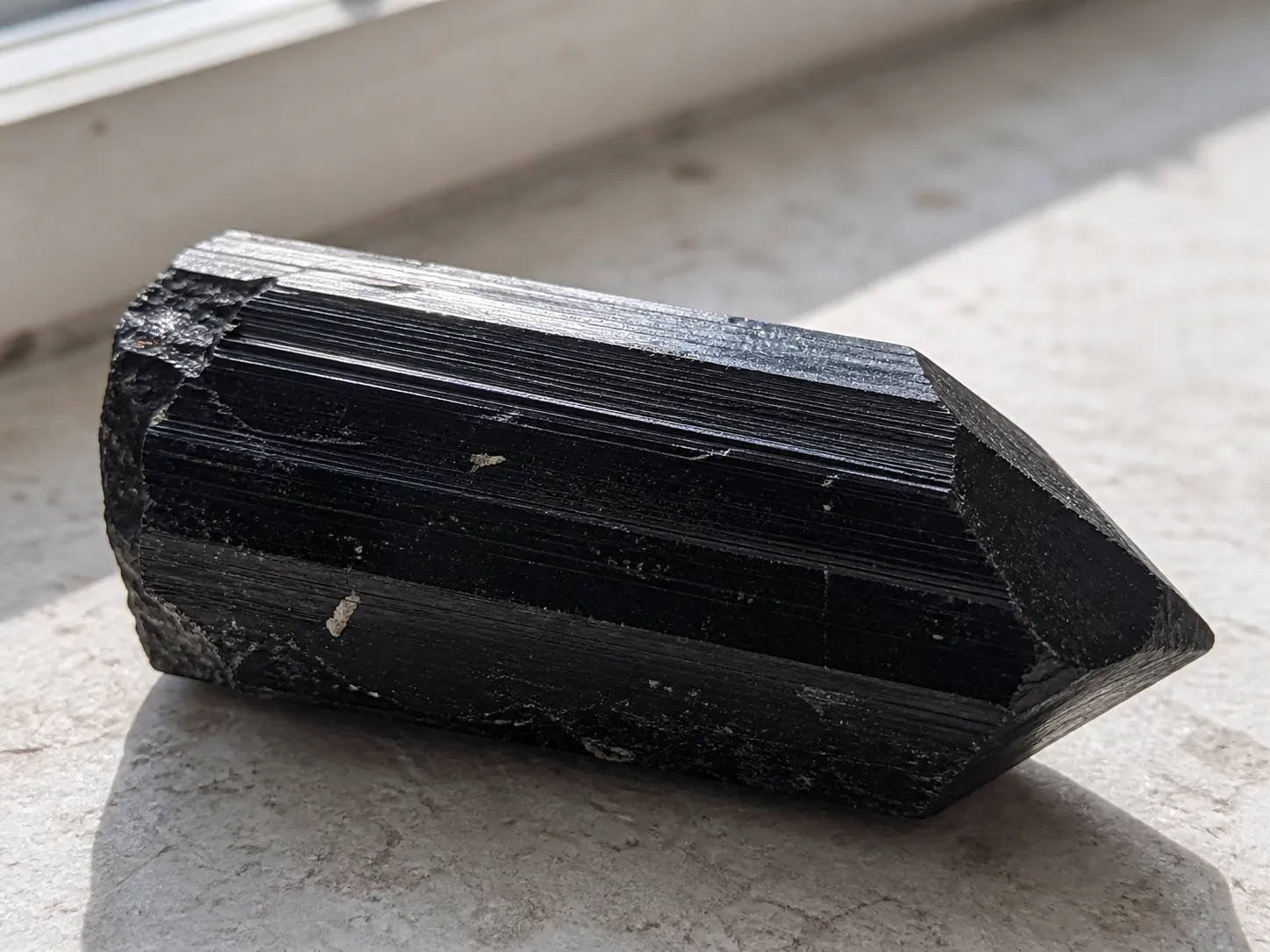 Raw black tourmaline point with a vulnerable thin edge and natural striations